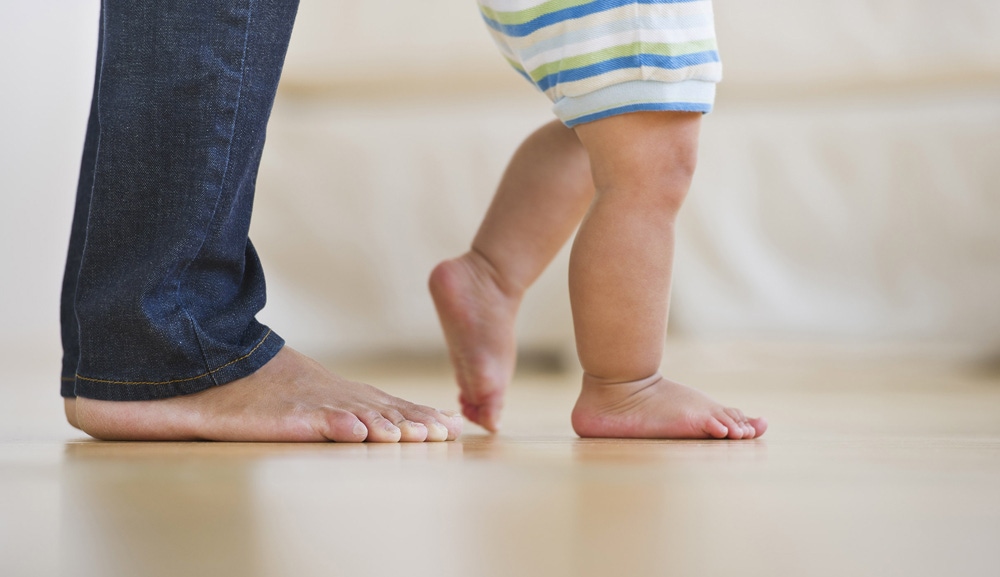 prim plan cu picioarele tatalui si al copilului care invata sa mearga
